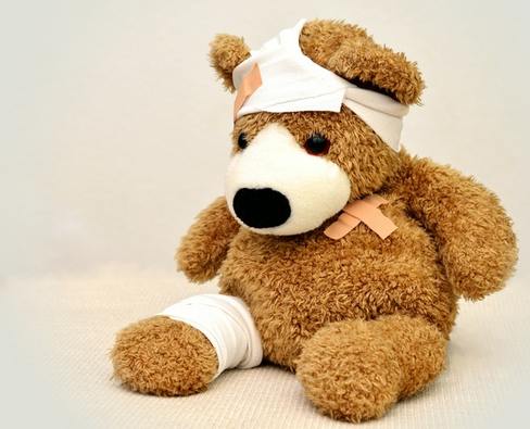Stuffed toy teddy bear with head and leg bandages, injured teddy bear
